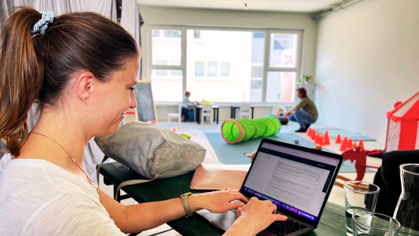 Frau mit Laptop im Vordergrund, dahinter spielende Kinder