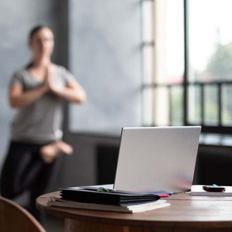 Im Vordergrund ein Laptop, im Hintergrund Yoga Ausübende