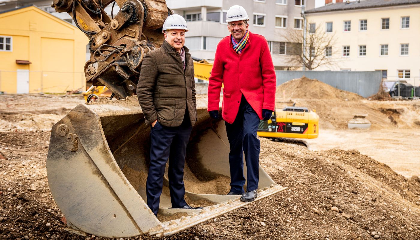 Gabor Wild und Tassilo Lang auf Baggerschaufel beim Spatenstich.